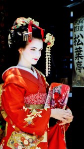 En geisha i rød kimono, hvitpudret ansikt og oppsatt hår.