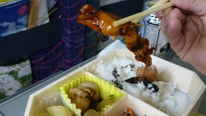 En syltet blekksprut holdes mellom to pinner. Under ser vi ris og andre ingredienser.