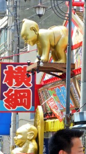 Gateskilt o Osaka med japanske tegn og en gullfarget sumobryter i plast.