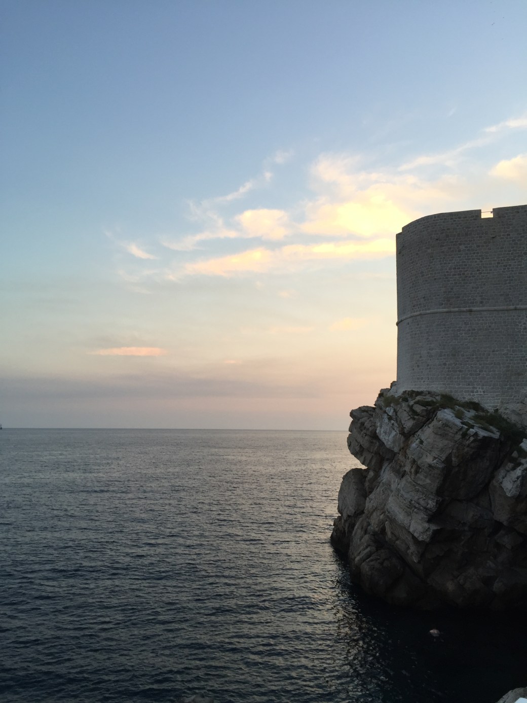 sjø, klippe med mur og solnedgang