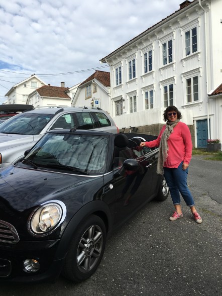 Svart mini cooper med dame i rosa genser ved siden av.